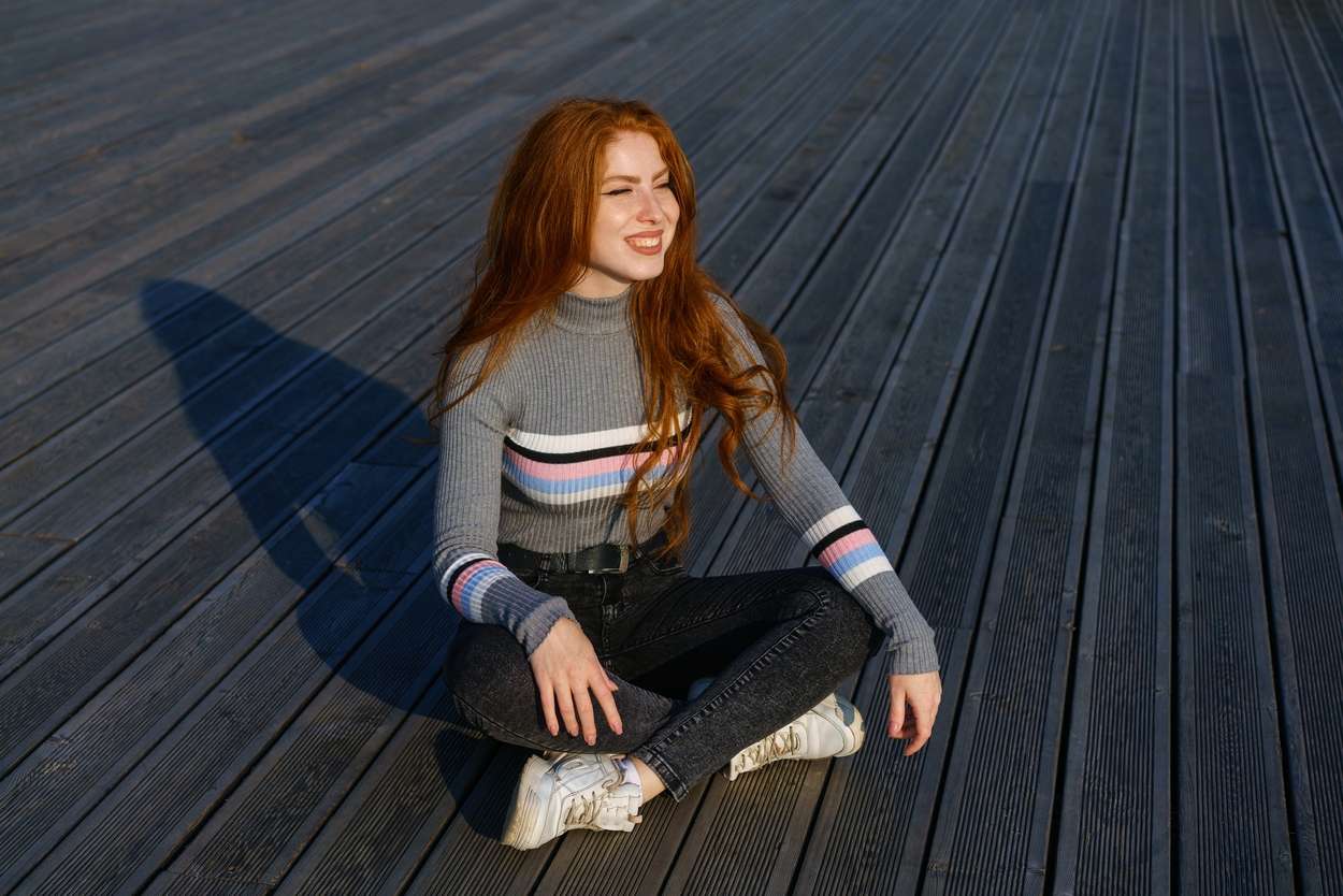 Happy young woman with red hair in the park on wooden flooring